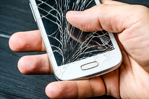 Main de l'homme sur son téléphone portable avec écran cassé dans l'obscurité. Téléphone intelligent avec écran tactile en verre brisé dans la main de l'homme. Fermer