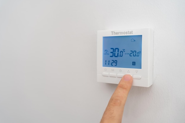 Main d'homme soulevant le thermostat de la climatisation pour réduire les coûts par la forte inflation