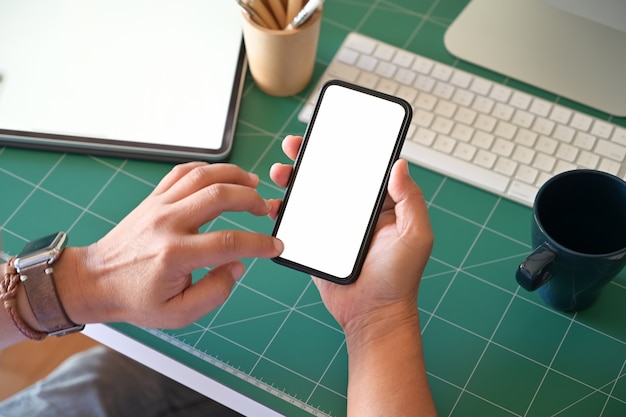 Main d&#39;homme sur téléphone intelligent mobile à écran blanc au lieu de travail.