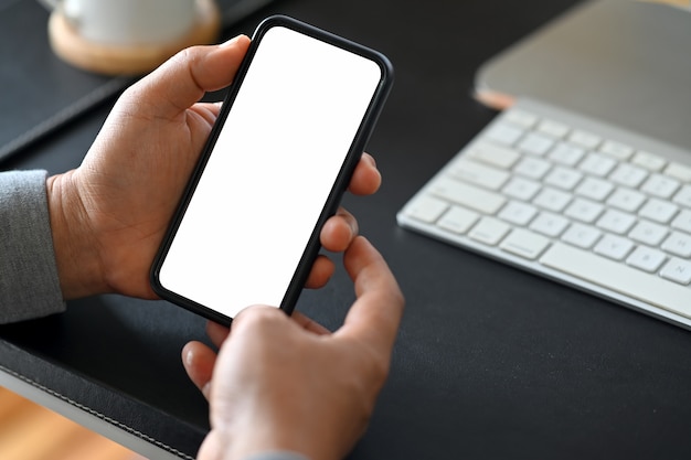 Main de l&#39;homme sur un téléphone mobile à écran blanc sur un bureau dans le bureau