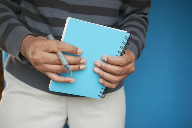 Main d'homme tenant un bloc-notes de couleur bleue avec un stylo