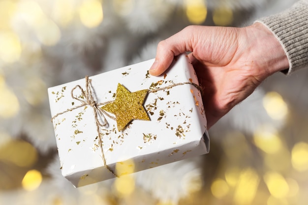 Main de l'homme tenant une boîte cadeau blanche avec étoile dorée, cadeau de Noël