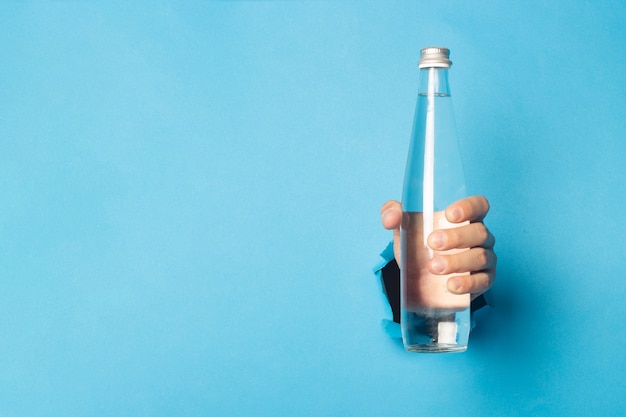 La main de l'homme tenant une bouteille en verre avec de l'eau sur un fond bleu clair