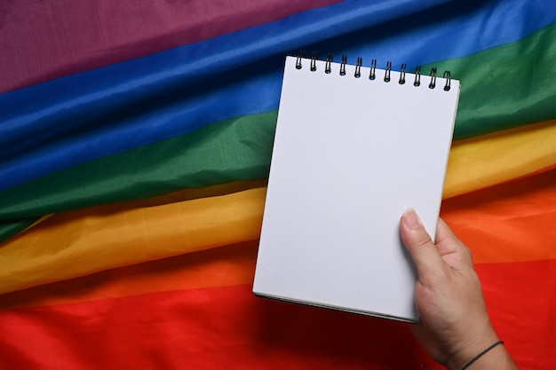 Main d'homme tenant un cahier vide sur le drapeau arc-en-ciel