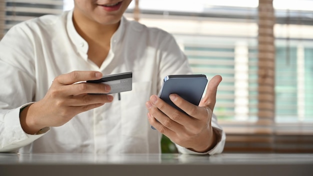 Main d'homme tenant une carte de crédit et un téléphone portable pour passer des commandes via Internet ou effectuer des transactions sur l'application bancaire mobile