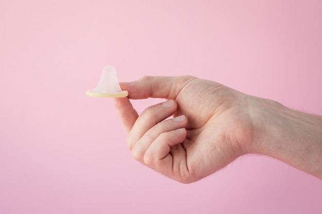 Main d'homme tenant un préservatif sur fond rose. Concept de contraception, prévention des infections sexuellement transmissibles et des grossesses non désirées.