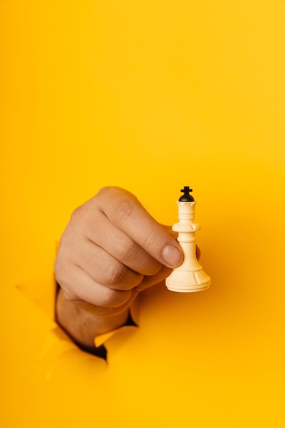 Main d'homme tenant le roi des échecs à travers un trou de fond jaune Image verticale