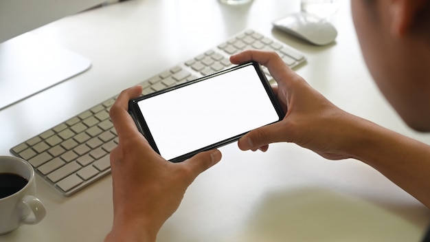 Main de l'homme tenant le smartphone avec écran blanc dans son bureau. Téléphone mobile à écran blanc pour le montage de l'affichage graphique.