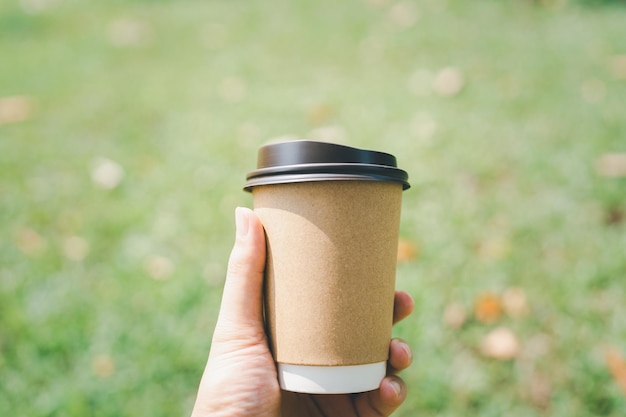 La main d'un homme tenant une tasse de café le matin avec fond d'herbe verte