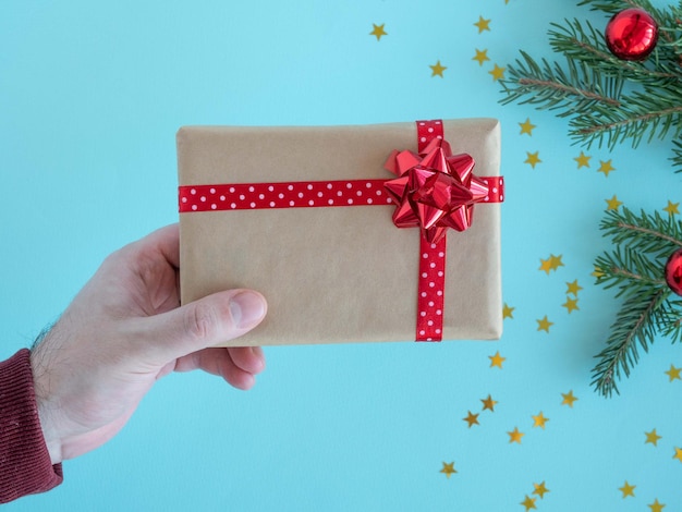 La main d'un homme tient une boîte-cadeau avec un arc rouge sur un fond de Noël.