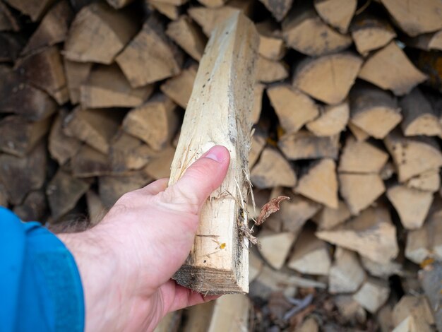 La main d'un homme tient une bûche tirée d'un tas de bois de chauffage