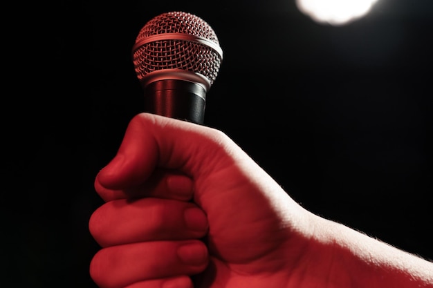 La main d'un homme tient un microphone professionnel sur fond de lumière de scène