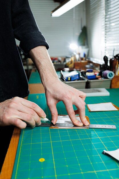 La main d'un homme tient des morceaux de cuir pour un portefeuille en cuir dans son atelier Le processus de travail avec du cuir marron naturel L'artisan tient l'artisanat