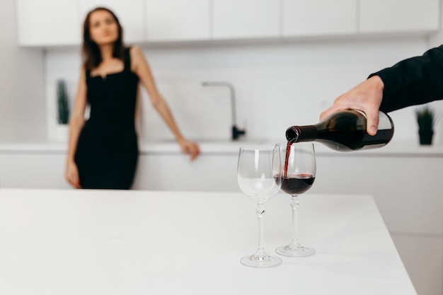 La main d'un homme verse du vin rouge dans des verres. Femme en arrière-plan