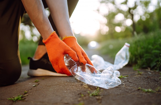 Photo la main des hommes recueille des ordures en plastique pour le nettoyage dans le parc. un volontaire portant des gants de protection recueille une bouteille en plastique.