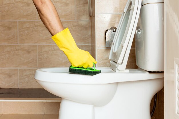 Photo une main humaine dans un gant en caoutchouc jaune utilise une brosse en plastique pour frotter le bol de toilette