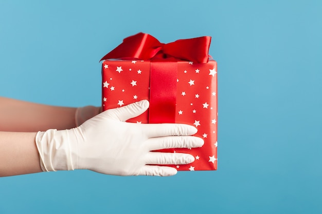 Main humaine dans des gants chirurgicaux blancs tenant une boîte cadeau rouge. concept de partage, de don ou de livraison.