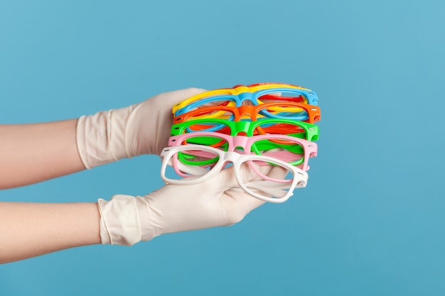 Main humaine dans des gants chirurgicaux blancs tenant et montrant de nombreuses lunettes colorées différentes.