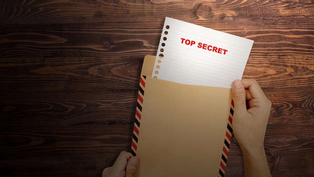 Une main humaine ouvre une enveloppe brune avec le texte de top secret sur le papier