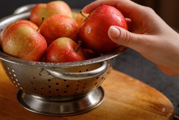 Photo la main humaine prend une pomme dans un bol métallique rempli de pommes mûres rouges. alimentation saine. ingrédients de la tarte aux pommes. cuisiner à la maison