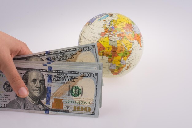 Main humaine tenant des billets en dollars américains à côté d'un globe modèle sur fond blanc
