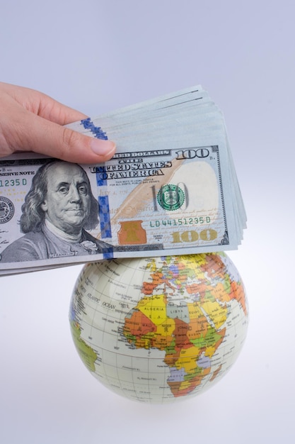Main humaine tenant des billets en dollars américains à côté d'un globe modèle