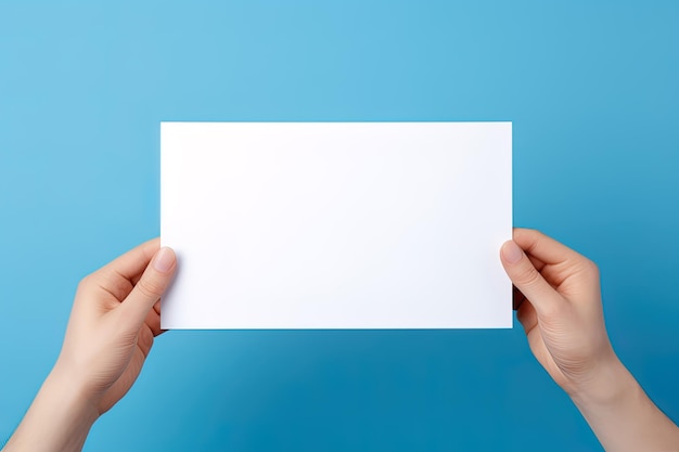 Une main humaine tenant une feuille vierge de papier blanc ou une carte isolée sur fond bleu