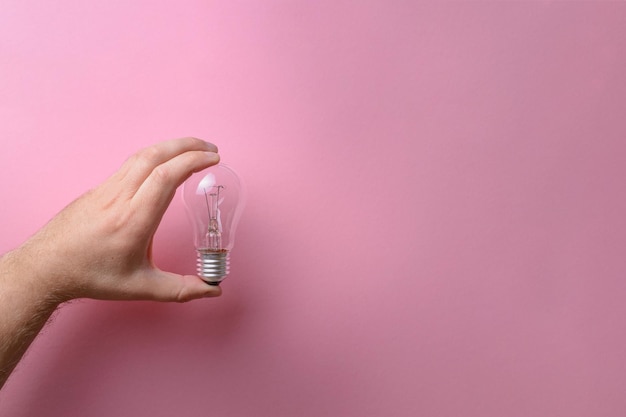 La main humaine tient une ampoule en verre sur fond rose Idées de créativité concepts d'inspiration