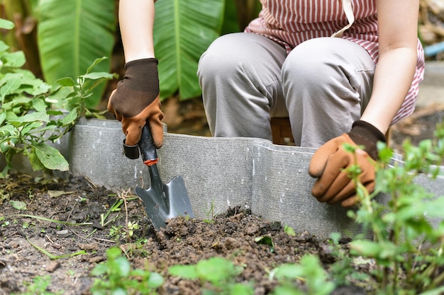 Main de jardinier plantant dans le jardin d'arrière-cour Femme en gants utilisant un outil de pelle à main pour les semis
