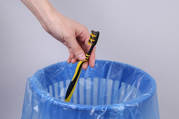 La main jette la brosse à dents en plastique dans la poubelle avec le paquet sur le fond gris