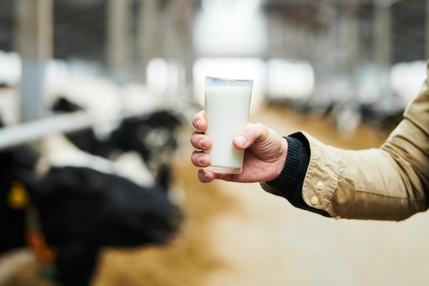 Main de jeune agriculteur de vache tenant un verre de lait frais