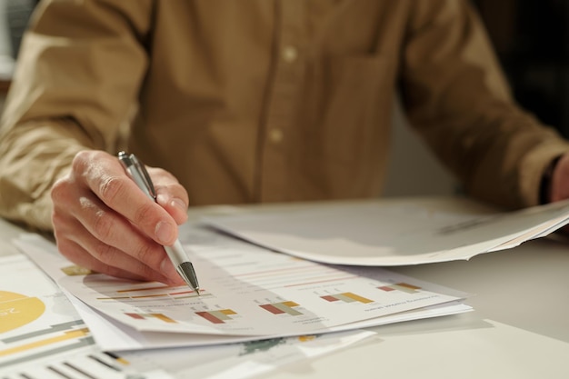 Main de jeune économiste avec un stylo pointant sur un document financier