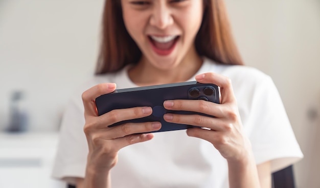 Main de jeune femme asiatique jouant à des jeux sur smartphone, loisirs de style de vie dans le salon à la maison.