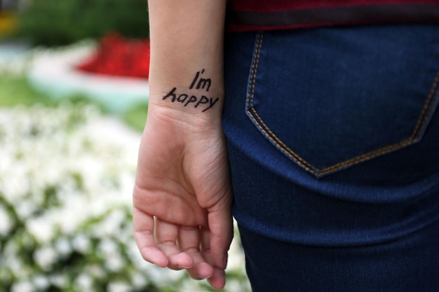 Main de jeune femme avec une phrase tatouée dessus sur fond de fleurs gros plan