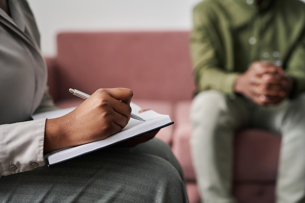 Main de jeune femme psychanalyste prenant des notes dans un cahier lors d'une session