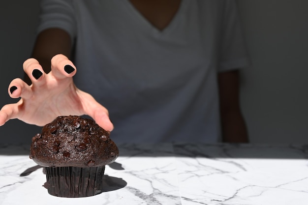 Main de jeune femme saisissant un muffin au chocolat