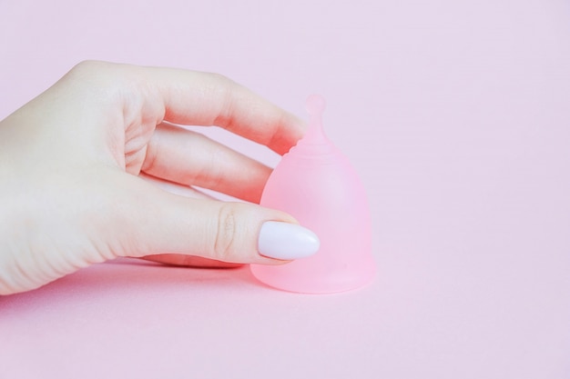 Main de jeune femme tenant la coupe menstruelle. Coupe menstruelle sur fond rose. Produit alternatif d&#39;hygiène féminine pendant la période. Concept de santé des femmes.