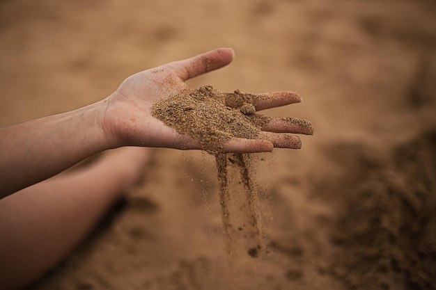 La main d'une jeune femme tient le sable du désert pendant le coucher du soleil