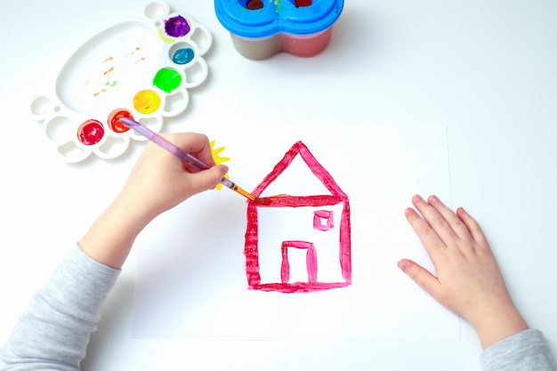 Main d'une jeune fille dessinant une maison rouge.