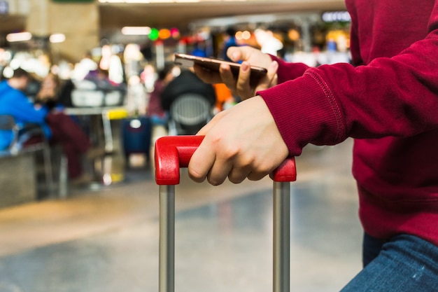 Main de la jeune fille se tenant la poignée de valise rouge