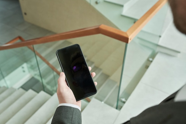 Main de jeune homme d'affaires tenant un smartphone dans le centre de bureau