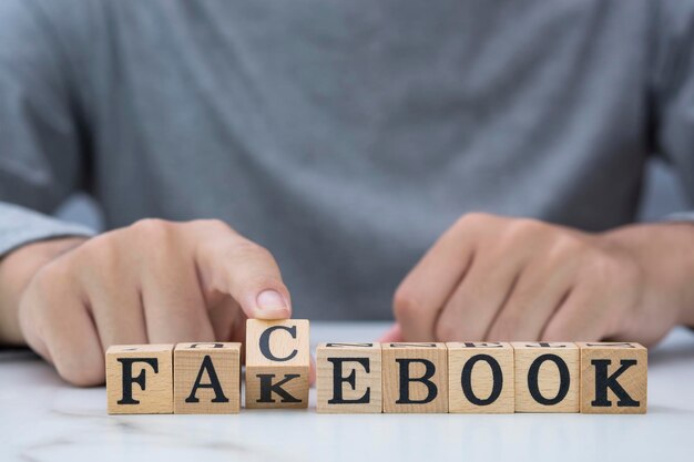 Main de jeune homme renversant des blocs cubiques en bois pour changer le libellé de fakebook en facebook