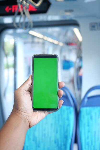 Main de jeune homme utilisant un téléphone intelligent avec écran vert à l'intérieur du métro