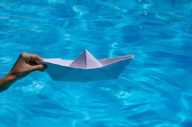 La main lance un bateau en papier blanc dans le bateau en papier origami d'eau de mer claire