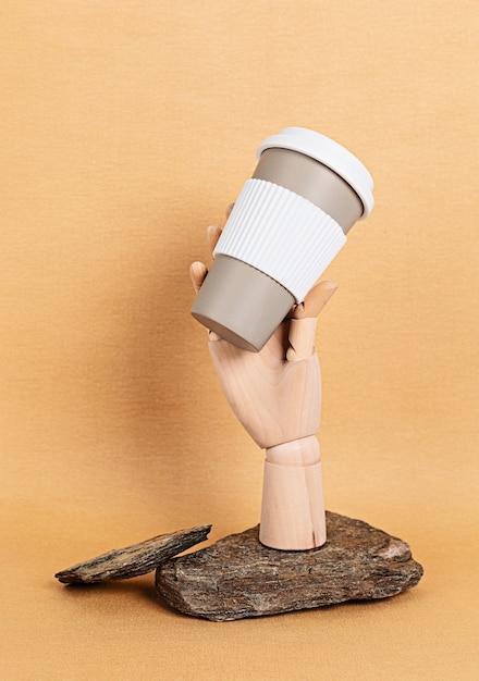 Main de mannequin en bois tenant une tasse de café réutilisable