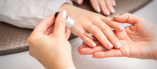 La main de la manucure verse l'huile à la pipette sur la cuticule des ongles de la jeune femme dans un salon de beauté. manucure française