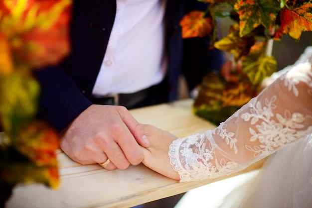 Main de marié avec anneau d'or tient la main de la mariée sur la surface en bois.