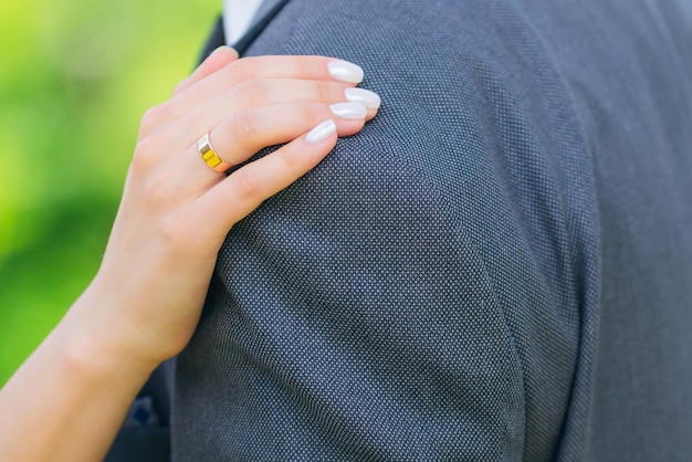 La main de la mariée avec une bague en or et une manucure douce se trouve sur le gros plan de l'épaule du marié