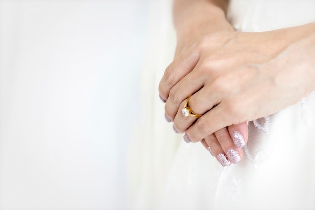 Main mariée avec belle bague en diamant sur une robe blanche.