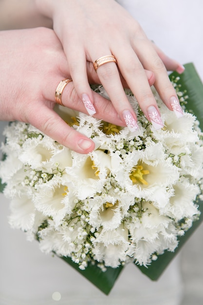 Main des mariés et bagues sur le bouquet de la mariée